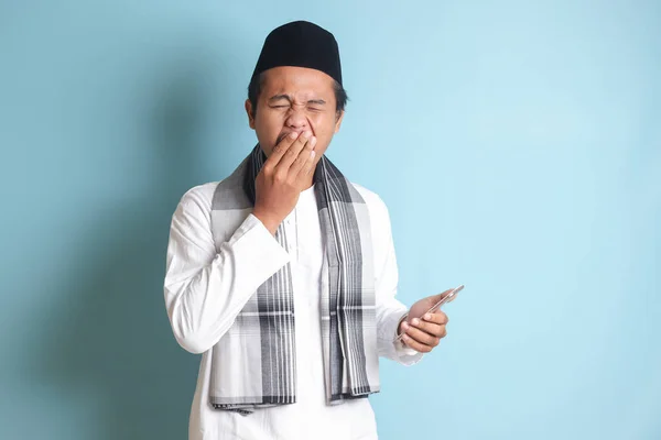 Retrato Del Joven Musulmán Asiático Sosteniendo Teléfono Móvil Mientras Bosteza — Foto de Stock