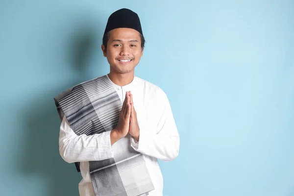 亚洲穆斯林男子的画像 身穿白色科科衬衫 头戴小帽 表示道歉和欢迎手势 蓝色背景上的孤立图像 — 图库照片