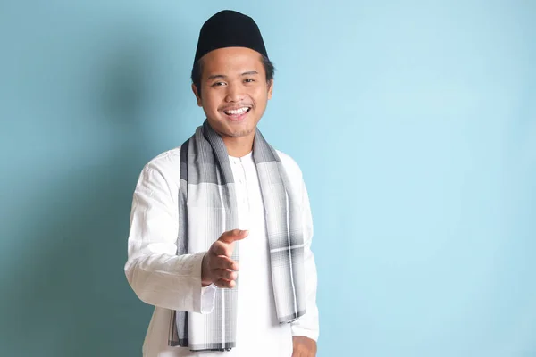 一位身穿白衬衫的迷人的亚洲穆斯林男子伸出手来握手 欢迎某个人的画像 蓝色背景上的孤立图像 — 图库照片