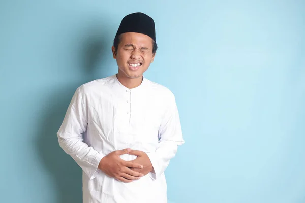 年轻的亚洲穆斯林男子的画像 他感到肚子痛 胃疼的概念 蓝色背景上的孤立图像 — 图库照片