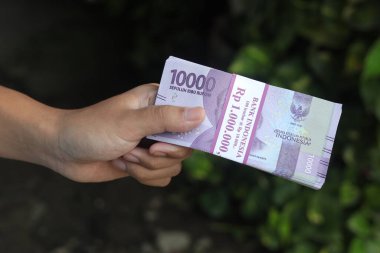 On bin rupiah banknot tutan bir erkek eli. Mali ve tasarruf kavramı