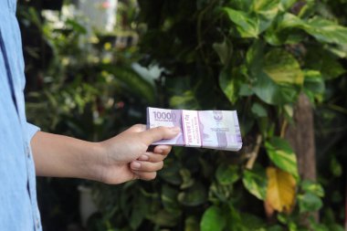On bin rupiah banknot tutan bir erkek eli. Mali ve tasarruf kavramı
