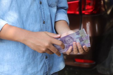 On bin rupiah banknot tutan bir erkek eli. Mali ve tasarruf kavramı