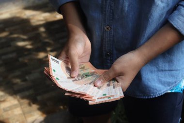 Beş bin rupia 'lık banknot tutan erkek eli yakın plan. Mali ve tasarruf kavramı