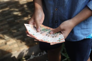 Beş bin rupia 'lık banknot tutan erkek eli yakın plan. Mali ve tasarruf kavramı