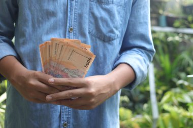 Beş bin rupia 'lık banknot tutan erkek eli yakın plan. Mali ve tasarruf kavramı