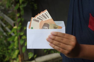 Erkek eli, zarfın içine beş bin rupiah para sıkıştırıyor. Mali ve tasarruf kavramı