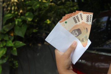 Erkek eli, zarfın içine beş bin rupiah para sıkıştırıyor. Mali ve tasarruf kavramı