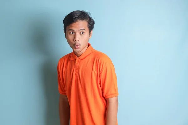 stock image surprised Asian man in orange shirt standing against blue background, showing shocked expression and looking aside