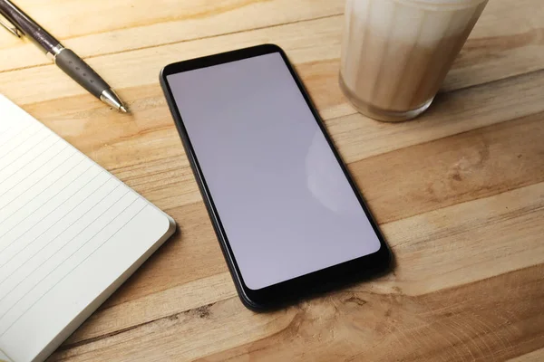 Boş ekran cep telefonu, boş defter, kalem ve gün boyunca bir fincan kahve. Ofis işi konsepti. Resimler düzleştirildi