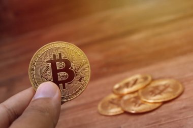 Erkek eli Bitcoin 'i tutarken yakın plan tahta masa arkasında bir yığın para ile. Kripto para ticareti kavramı