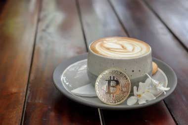 Kafedeki ahşap masada bitcoin ile bir fincan cappuccino. Kripto para ticareti kavramı