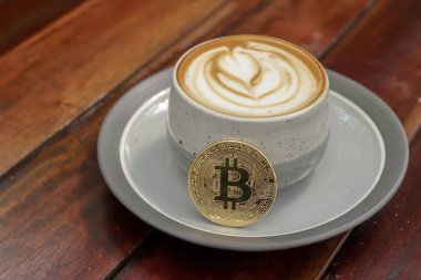 Kafedeki ahşap masada bitcoin ile bir fincan cappuccino. Kripto para ticareti kavramı