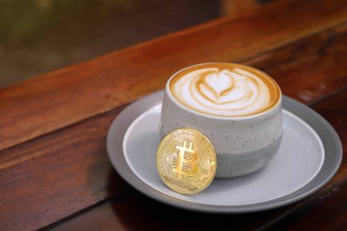 Kafedeki ahşap masada bitcoin ile bir fincan cappuccino. Kripto para ticareti kavramı
