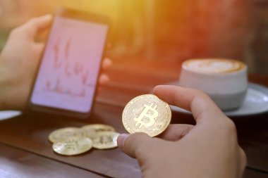 Erkek elinin Bitcoin ve cep telefonuyla ekranda şamdan çizelgesini tutarken yaklaş. Kripto para ticareti kavramı