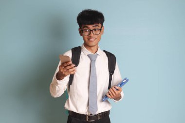 Endonezyalı lise öğrencisi beyaz gömlek giyiyor ve gri kravat takıyor cep telefonu tutarken şok olmuş yüz ifadesi gösteriyor. Beyaz arkaplanda izole edilmiş resim