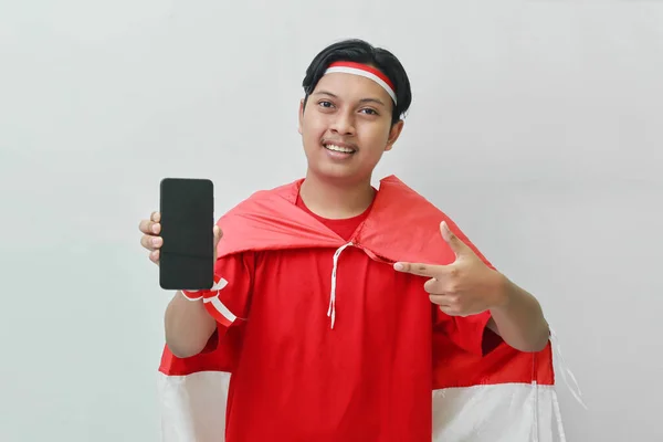 身穿T恤 头戴红白缎带 肩上挂着国旗 头戴斗篷 手持空白屏幕手机的亚洲男子的画像 灰色背景上的孤立图像 — 图库照片