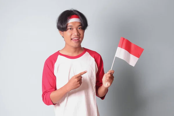 インドネシアの旗を掲げながら 赤と白のリボンでTシャツを着た魅力的なアジア人男性の肖像画 灰色の背景に隔離された画像 — ストック写真