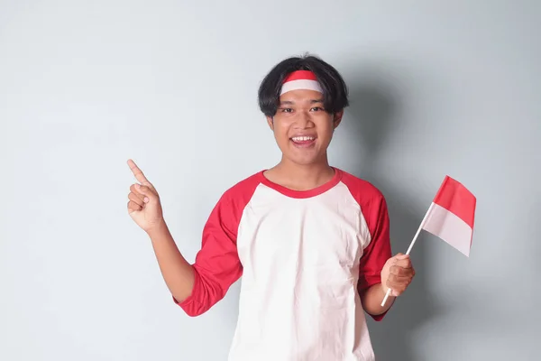 头戴红白相间的T恤衫 展示亚洲男子的形象 一边展示产品 一边拉着印尼盾 一边垂头丧气 灰色背景上的孤立图像 — 图库照片