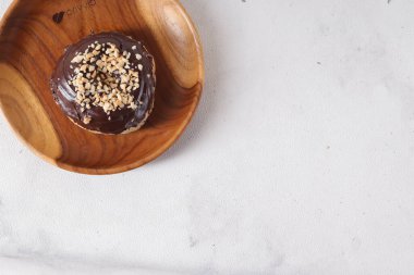 Tahta tabakta servis edilen fındıklı fındıklı tatlı çikolata kaplı donut. Beyaz arkaplanda izole edilmiş resim