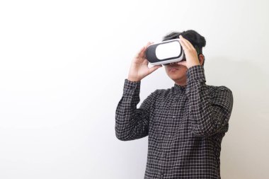 Siyah ekose gömlekli Asyalı bir adamın Sanal Gerçeklik (VR) gözlüklerini takıp yukarı bakarken portresi. Beyaz arkaplanda izole edilmiş resim