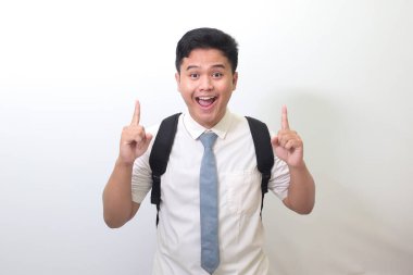 Endonezyalı lise öğrencisi beyaz gömlekli, gri kravatlı bir şey gösteriyor ve gülümsüyor. Beyaz arkaplanda izole edilmiş resim