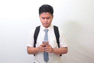Endonezyalı lise öğrencisi beyaz gömlekli, gri kravatlı cep telefonu tutarken yüzünün allak bullak olduğunu gösteriyor. Beyaz arkaplanda izole edilmiş resim