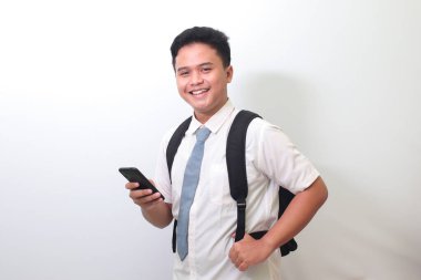 Endonezyalı lise öğrencisi beyaz gömlek giyiyor ve gri kravat takıyor cep telefonu tutarken şok olmuş yüz ifadesi gösteriyor. Beyaz arkaplanda izole edilmiş resim