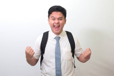 Endonezyalı lise öğrencisi beyaz gömlekli, gri kravatlı, yumruğunu kaldırıp başarısını kutluyor. Yarışma konseptini kazanmak. Beyaz arkaplanda izole edilmiş resim