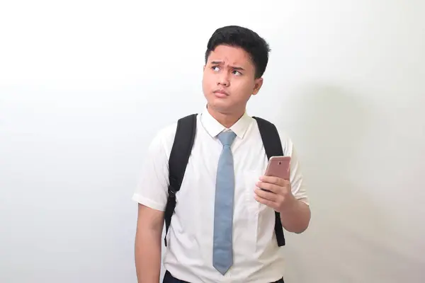 印尼高中学生穿着白色衬衫制服 灰色领带 手持手机时面部表情混乱 白色背景上的孤立图像 — 图库照片