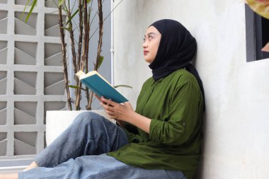 Balkonda kitap okuyan Asyalı çekici kadının portresi. Müslüman kız boş zamanın tadını çıkarıyor. Okuryazarlık ve bilgi kavramı