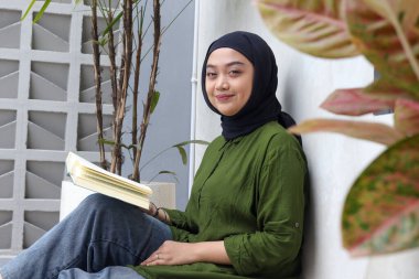 Balkonda kitap okuyan Asyalı çekici kadının portresi. Müslüman kız boş zamanın tadını çıkarıyor. Okuryazarlık ve bilgi kavramı