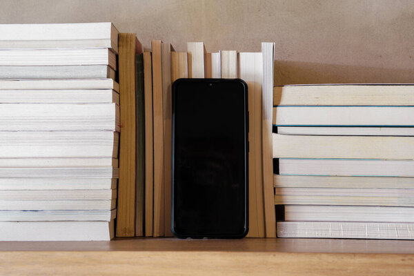 Stack of books on wooden bookshelf with blank screen smartphone in middle. Education and knowledge concept