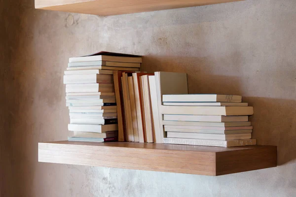 Stack of books on floating wooden bookshelf. Education and knowledge concept. Pile of books to read. House interior decoration