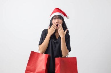 Kırmızı Noel Baba şapkalı şaşırmış Asyalı kadının portresi bir şeyler alırken mutlu oluyor. Alışveriş çantası tutan heyecanlı kız. Yeni yıl ve Noel konsepti. Beyaz arkaplanda izole edilmiş resim