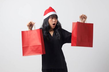 Kırmızı Noel Baba şapkalı şaşırmış Asyalı kadının portresi bir şeyler alırken mutlu oluyor. Alışveriş çantası tutan heyecanlı kız. Yeni yıl ve Noel konsepti. Beyaz arkaplanda izole edilmiş resim