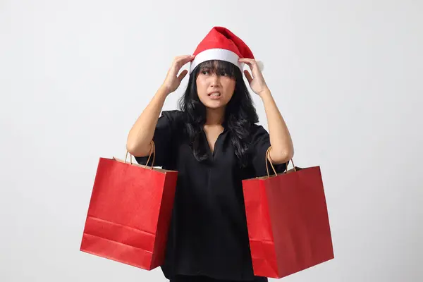 Kırmızı Noel Baba şapkalı şaşırmış Asyalı kadının portresi bir şeyler alırken mutlu oluyor. Alışveriş çantası tutan heyecanlı kız. Yeni yıl ve Noel konsepti. Beyaz arkaplanda izole edilmiş resim