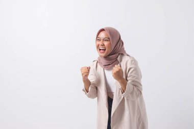 Heyecanlı Asyalı tesettürlü kadın resmi. Sıradan giyinmiş, yumruğunu kaldırmış, başarıyı kutluyor. İş kadını konsepti. Beyaz arkaplanda izole edilmiş resim