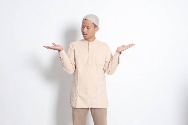 Kafası karışmış Koko gömlekli Asyalı Müslüman adamın portresi. Kafatası yana doğru açılmış ve iki şey tutuyor. Ürünleri gösteriyor. Beyaz arkaplanda izole edilmiş resim