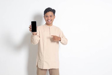 Koko tişörtlü heyecanlı Asyalı Müslüman adamın portresi ürünü gösterip sunarken boş ekran cep telefonu modeli gösteriyor. Sosyal medya konsepti. Beyaz arkaplanda izole edilmiş resim