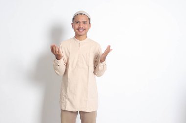 Koko gömlekli, dindar Asyalı Müslüman bir adamın portresi. Kafatası şapkalı, elleri havada dua ediyor. Dindar inanç konsepti. Beyaz arkaplanda izole edilmiş resim