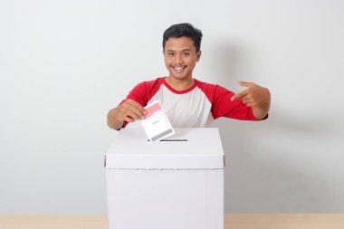Heyecanlı Asyalı adamın portresi oy pusulasını sandığa yerleştirip koyuyor. Endonezya cumhurbaşkanı ve hükümeti için genel seçimler veya Pemilu. Beyaz arkaplanda izole edilmiş resim