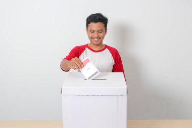 Heyecanlı Asyalı adamın portresi oy pusulasını sandığa yerleştirip koyuyor. Endonezya cumhurbaşkanı ve hükümeti için genel seçimler veya Pemilu. Beyaz arkaplanda izole edilmiş resim