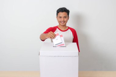 Heyecanlı Asyalı adamın portresi oy pusulasını sandığa yerleştirip koyuyor. Endonezya cumhurbaşkanı ve hükümeti için genel seçimler veya Pemilu. Beyaz arkaplanda izole edilmiş resim