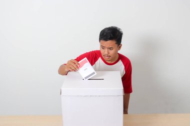 Heyecanlı Asyalı adamın portresi oy pusulasını sandığa yerleştirip koyuyor. Endonezya cumhurbaşkanı ve hükümeti için genel seçimler veya Pemilu. Beyaz arkaplanda izole edilmiş resim