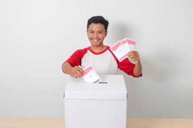 Heyecanlı Asyalı adamın portresi oy pusulasını sandığa yerleştirip koyuyor. Endonezya cumhurbaşkanı ve hükümeti için genel seçimler veya Pemilu. Beyaz arkaplanda izole edilmiş resim