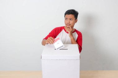 Heyecanlı Asyalı adamın portresi oy pusulasını sandığa yerleştirip koyuyor. Endonezya cumhurbaşkanı ve hükümeti için genel seçimler veya Pemilu. Beyaz arkaplanda izole edilmiş resim