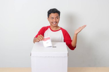 Heyecanlı Asyalı adamın portresi oy pusulasını sandığa yerleştirip koyuyor. Endonezya cumhurbaşkanı ve hükümeti için genel seçimler veya Pemilu. Beyaz arkaplanda izole edilmiş resim