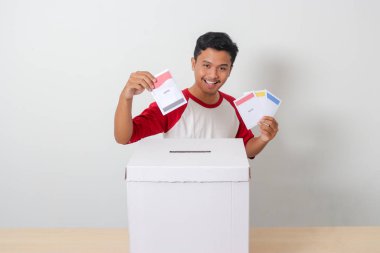 Heyecanlı Asyalı adamın portresi oy pusulasını sandığa yerleştirip koyuyor. Endonezya cumhurbaşkanı ve hükümeti için genel seçimler veya Pemilu. Beyaz arkaplanda izole edilmiş resim