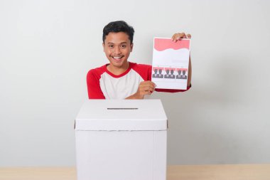 Heyecanlı Asyalı adamın portresi oy pusulasını sandığa yerleştirip koyuyor. Endonezya cumhurbaşkanı ve hükümeti için genel seçimler veya Pemilu. Beyaz arkaplanda izole edilmiş resim
